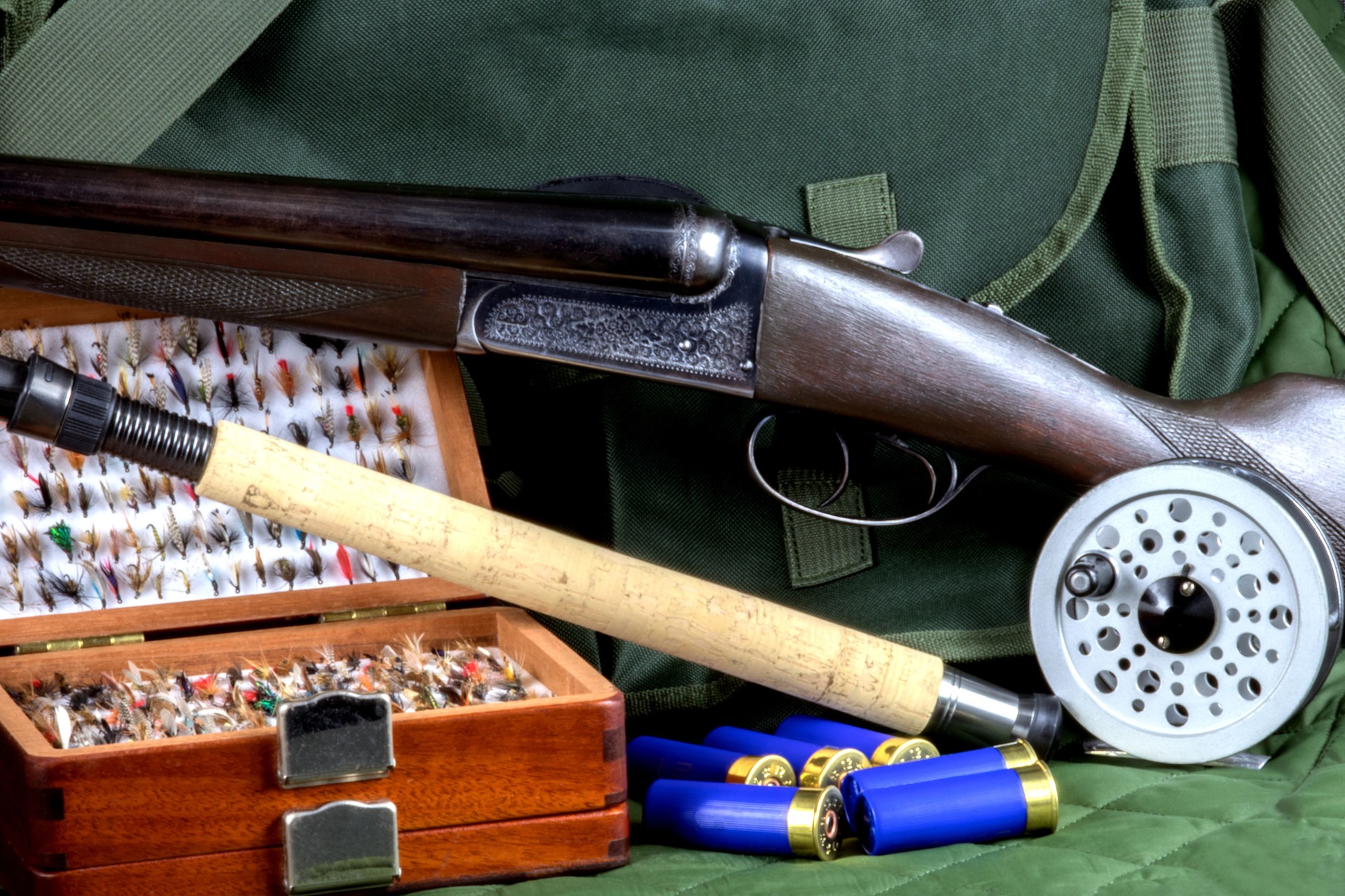 Shotgun with Fishing Rod and Fly Box and Fly Reel and Cartridges with Game Bag on an Outdoor Coat