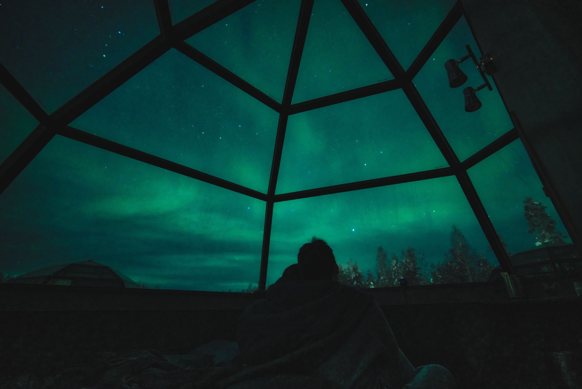 A couple enjoy view of Aurora Borealis and stars in glass igloo in Lapland, Rovaniemi, Finland
