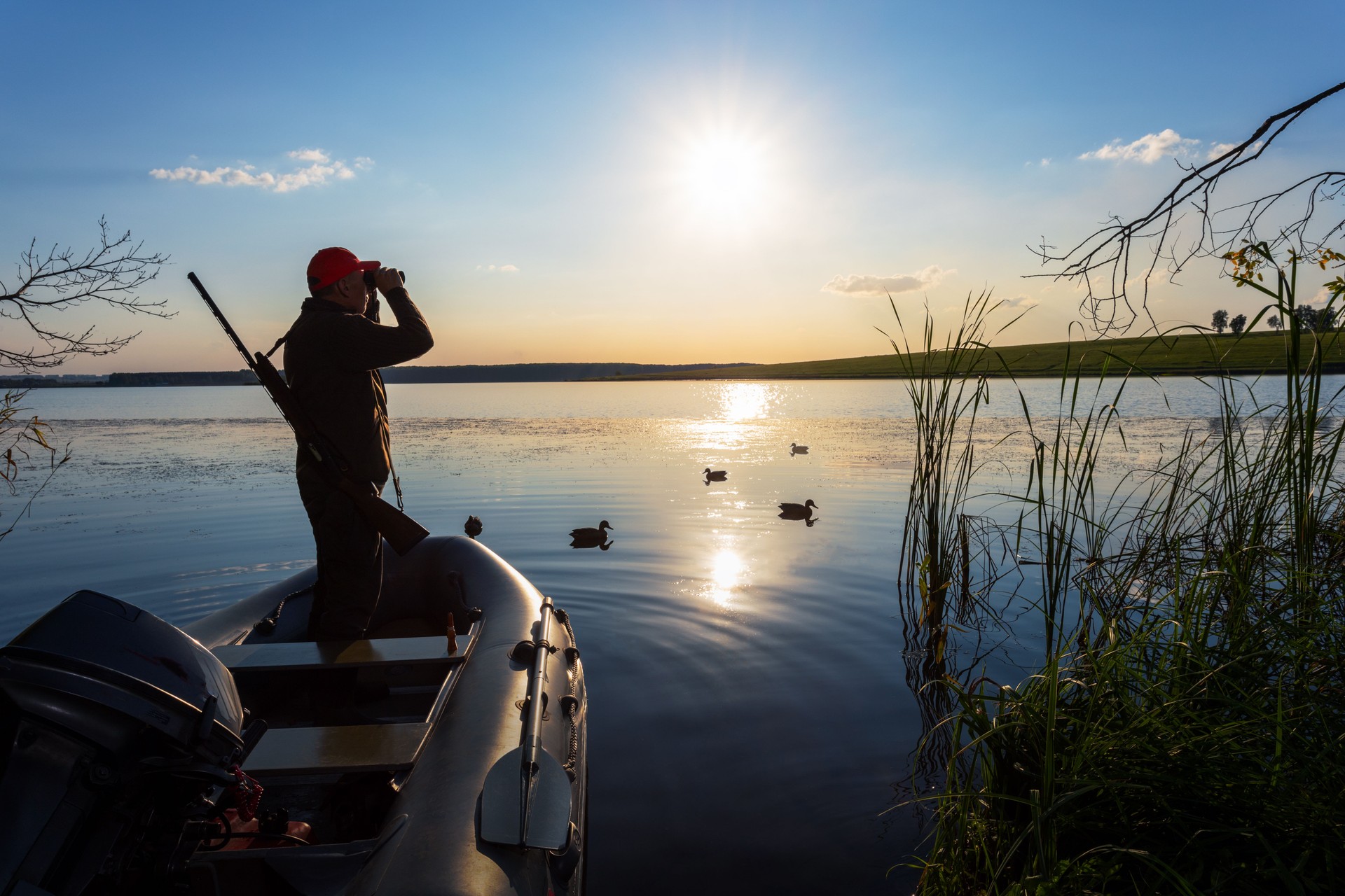 Hunter looks through binoculars at the sky at lake.  duck hunting at sunrise.
